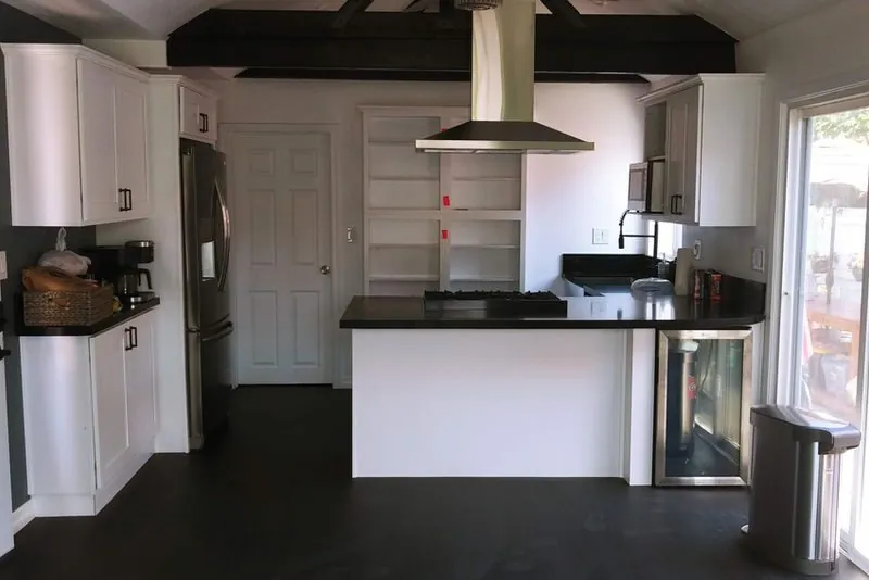 Open kitchen with peninsula, island hood, dark counters and exposed painted beams