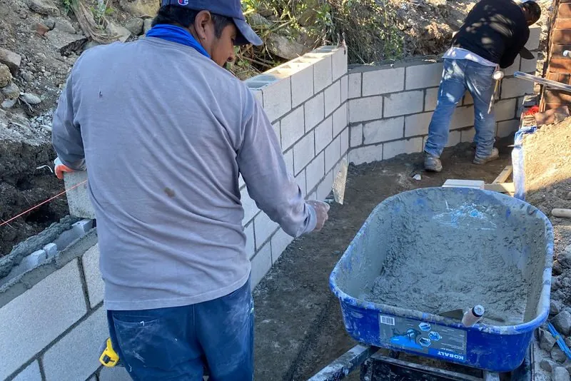 Two masons laying concrete block for a reinforced retaining wall on a hillside cut