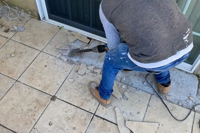 Worker breaking out a failed tile patio surface with a demolition hammer