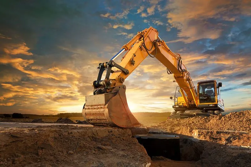 Tracked excavator cutting a utility trench across a graded construction site