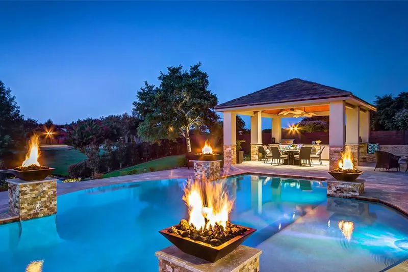 Completed swimming pool with raised water features and integrated fire bowls at dusk