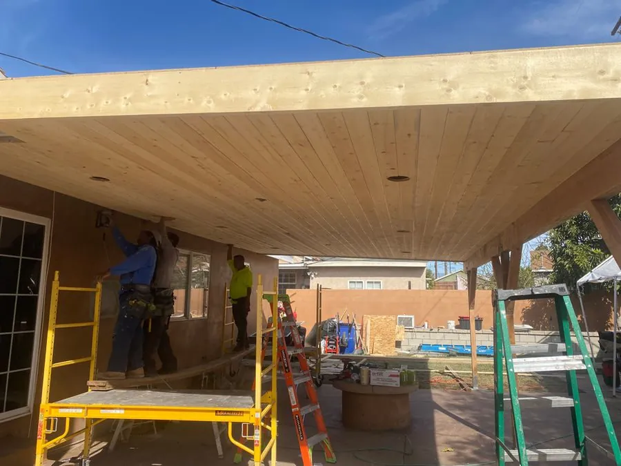 Tad's Construction crew installing the ceiling of a wood patio cover from scaffolding