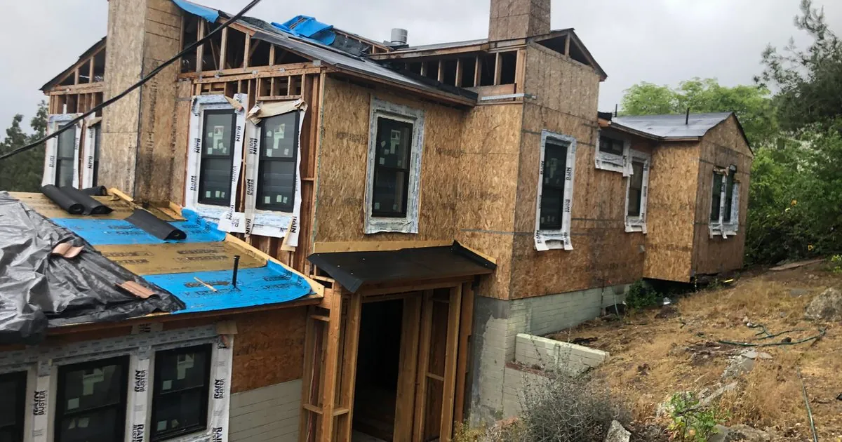 Two-story wood-framed structure under construction with weather barrier installed